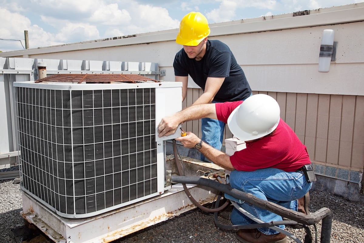 Two workers on the roof of a building working on the air conditioning unit.