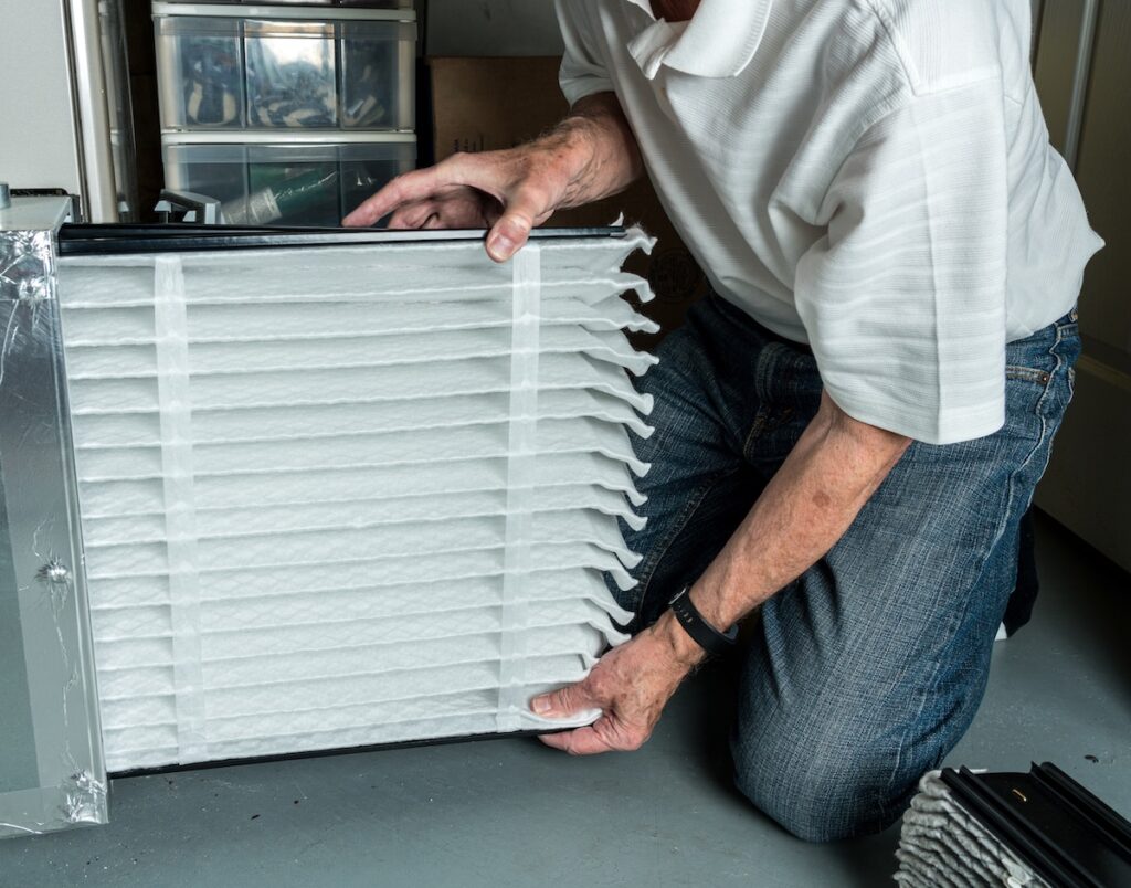 how to maintain heating and air conditioning Senior caucasian man checking a clean folded air filter in the HVAC furnace system in basement of home