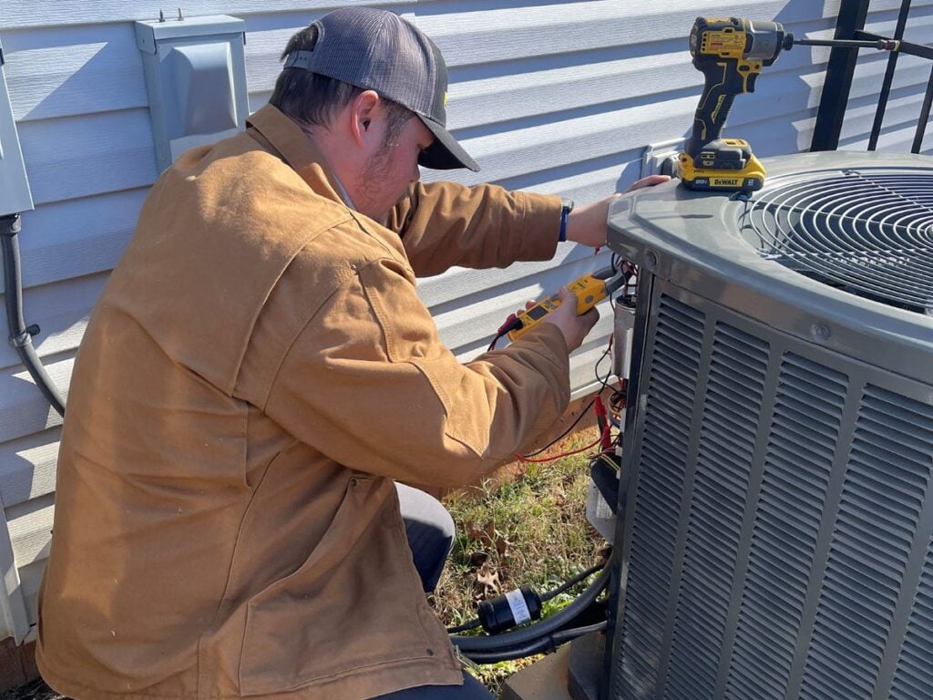 worker repairing unit outside heat pump blowing cold air