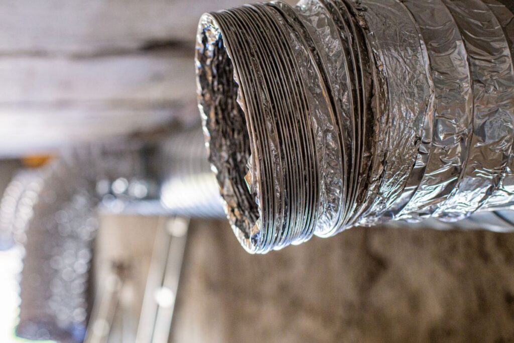 A close-up view of a dirty air vent and flexible duct attached to a building's ceiling.