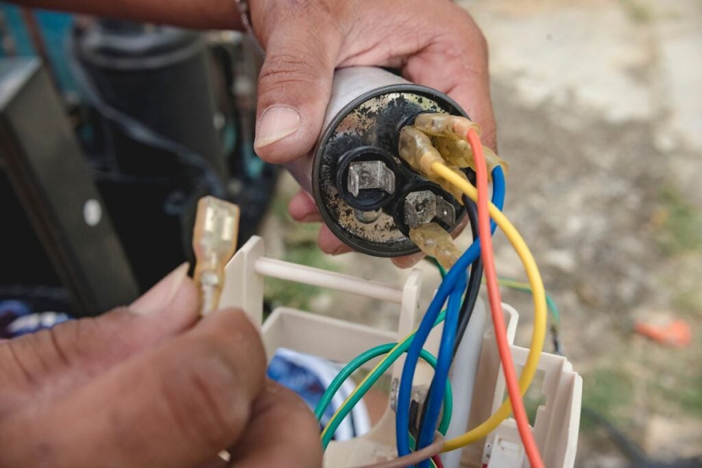 An AC technician removes a defective capacitor from a window type air conditioner control panel
