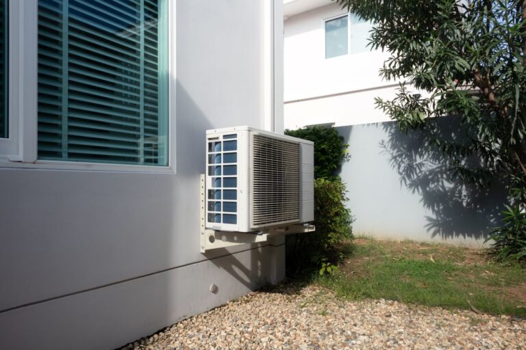 Outdoor air conditioning unit on side of residential house, system mounted on exterior wall