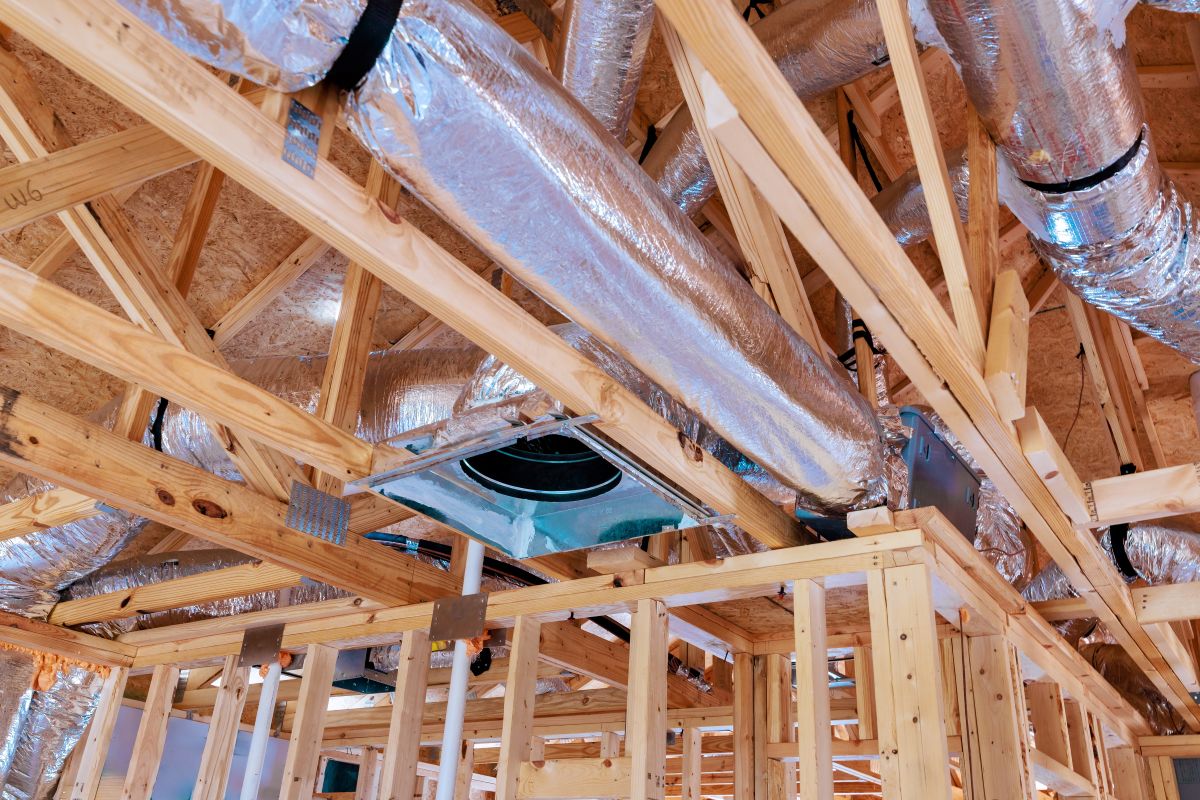 Construction workers install ductwork framing for residential ceiling in newly built home during works day
