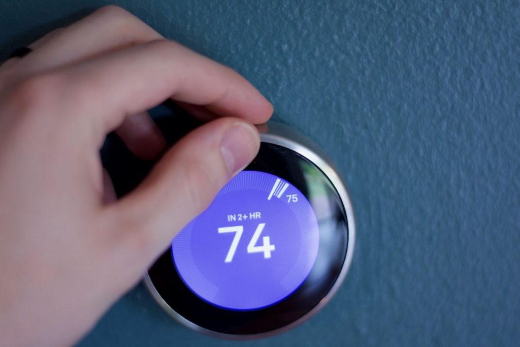 Hand changes temperature of smart home thermostat on blue wall in Fahrenheit